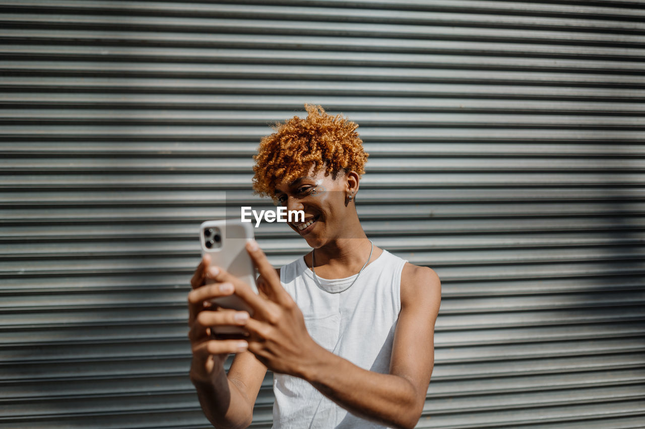 Young dark-skinned man posing at the street and taking selfie in the city background