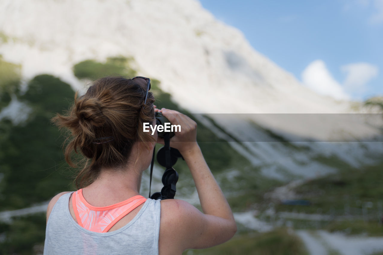 Rear view of woman looking through binoculars against mountains