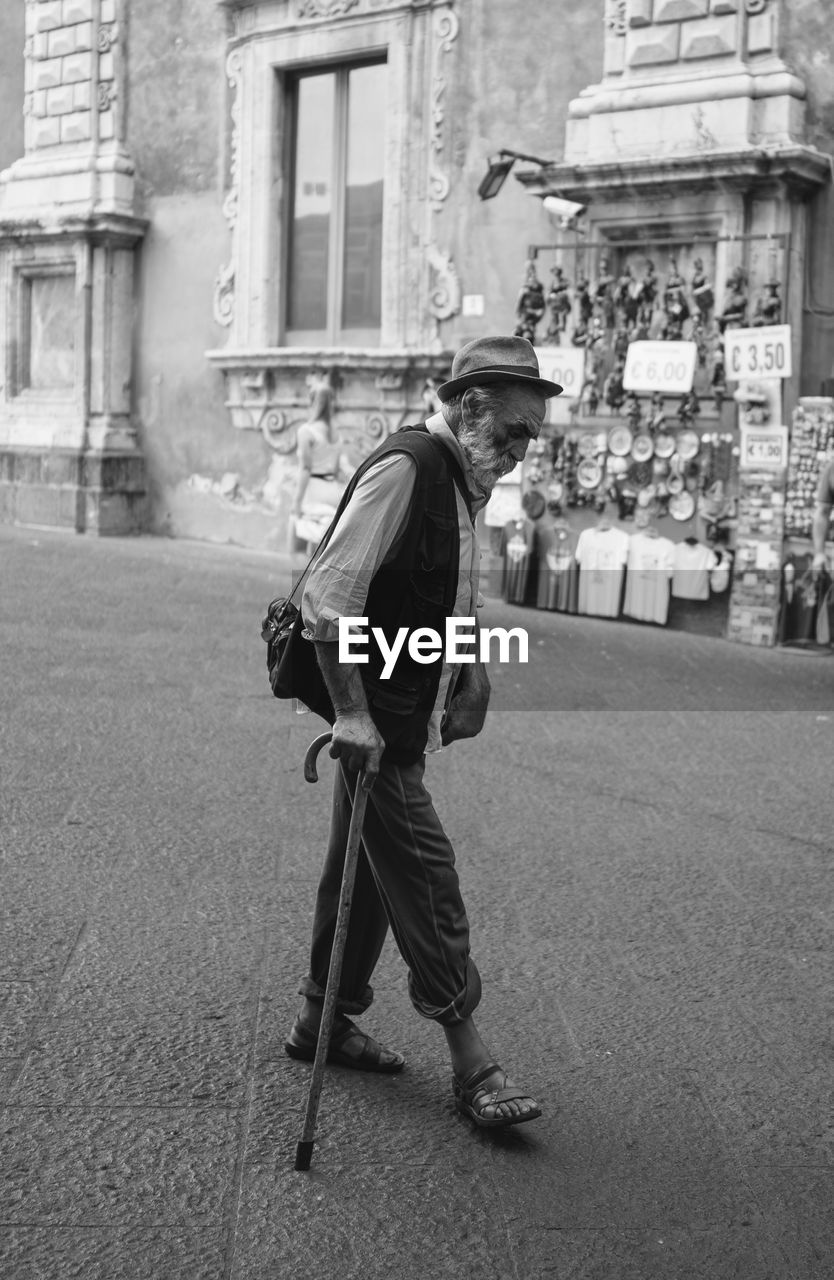 FULL LENGTH SIDE VIEW OF MAN WALKING ON STREET AGAINST BUILDINGS