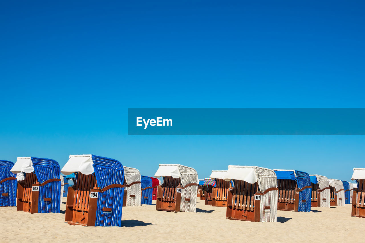 Hooded chairs at beach against clear blue sky during sunny day