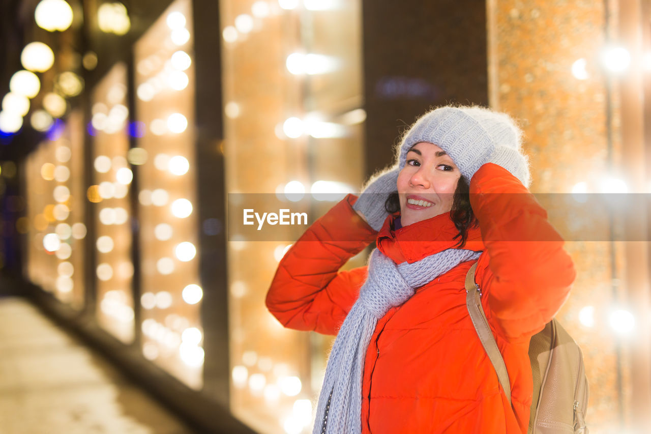 PORTRAIT OF SMILING WOMAN STANDING AT ILLUMINATED SNOW