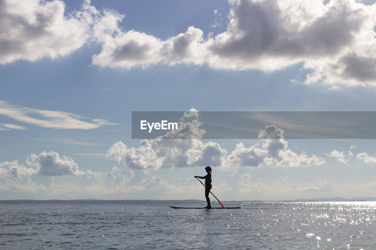 Woman paddleboarding in sea against sky