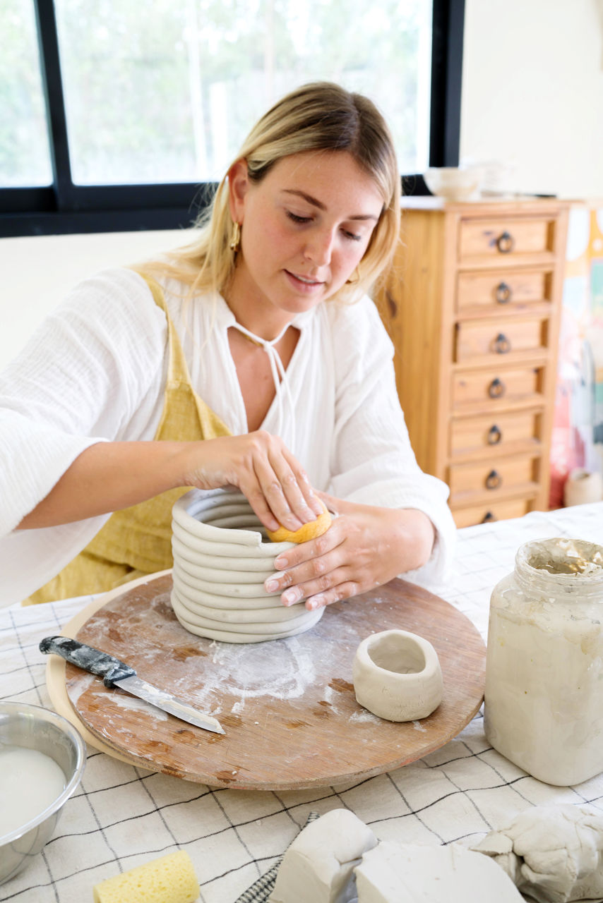 Female pottery artist making a vase in her home studio