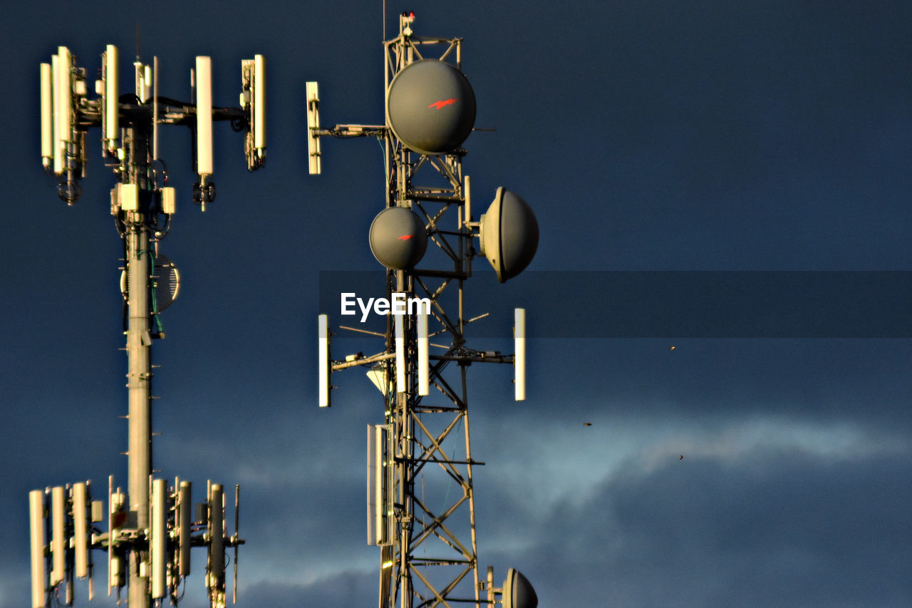 Low angle view of repeater towers against cloudy sky