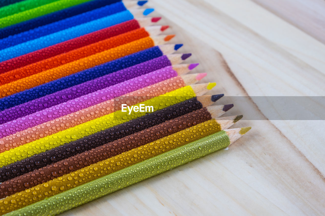 Multicolored pencils with water drops on wooden table, top view, selective focus