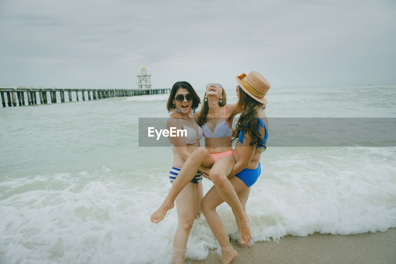 Women lifting friend at beach against sky