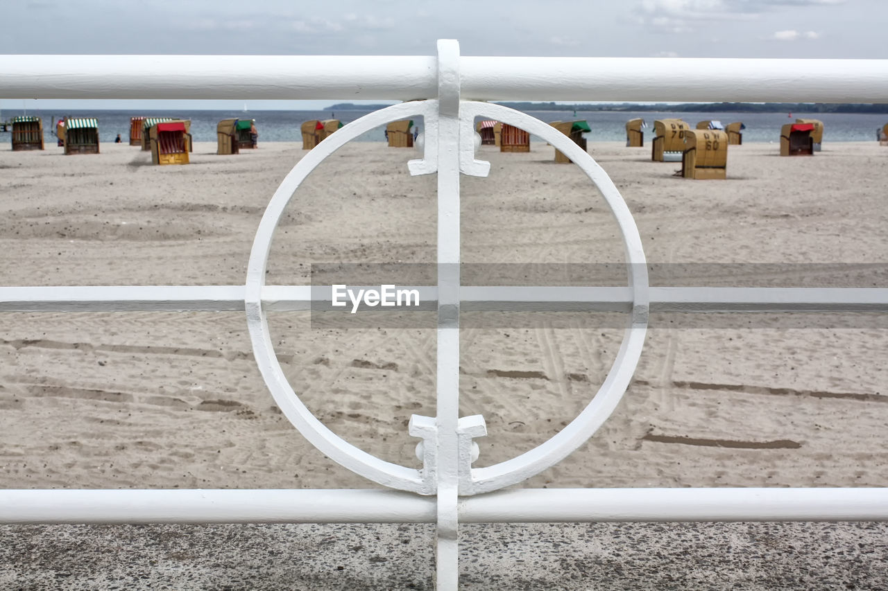 Hooded chairs at beach seen through white railing