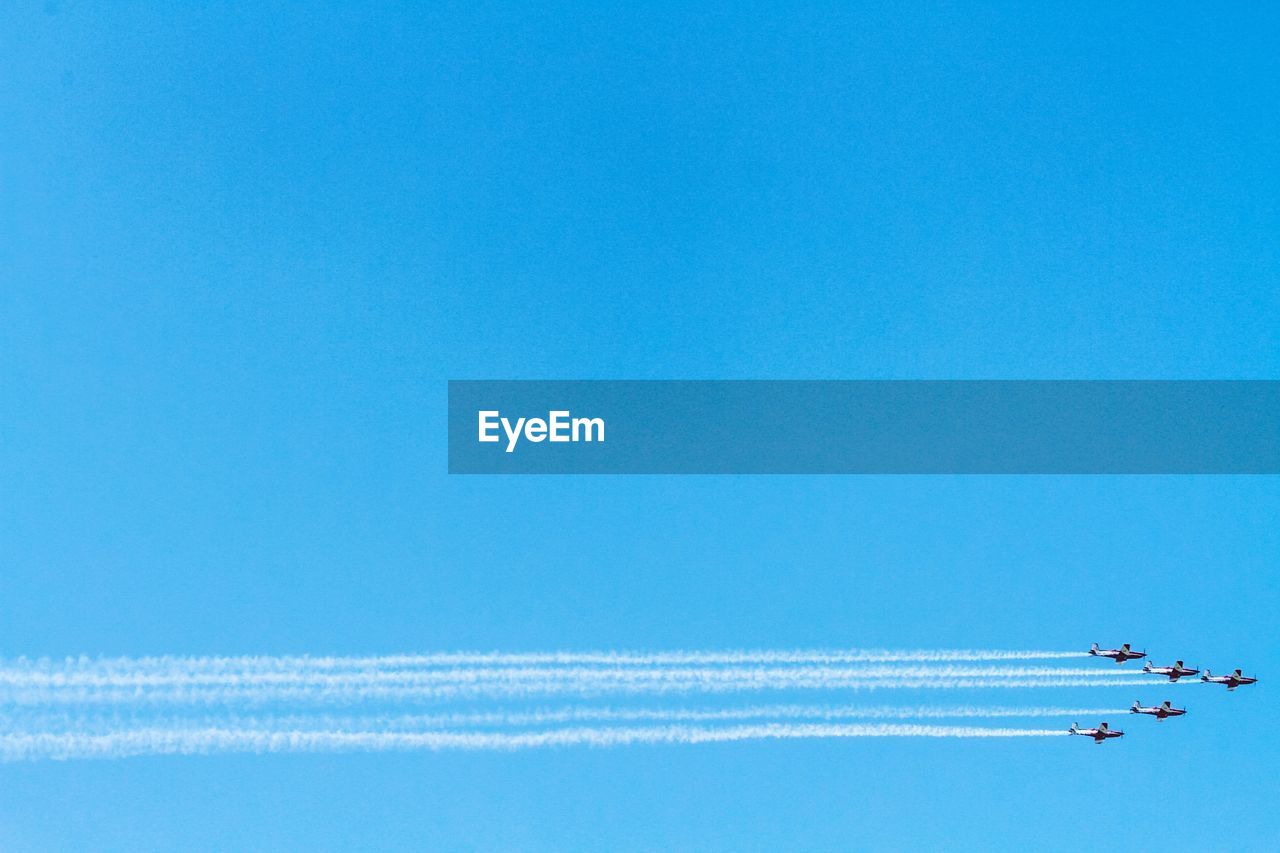 Low angle view of airplanes flying against clear blue sky