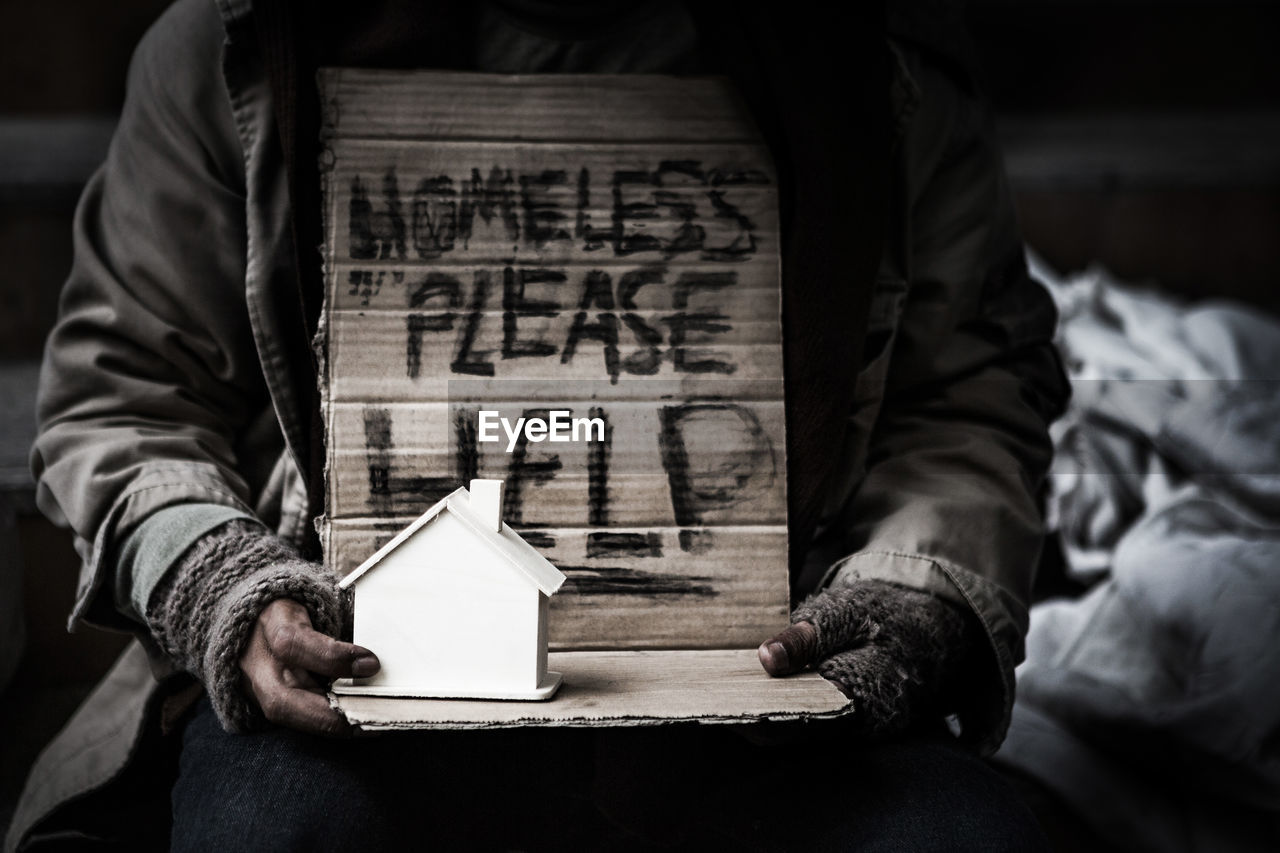 Midsection of beggar with model house