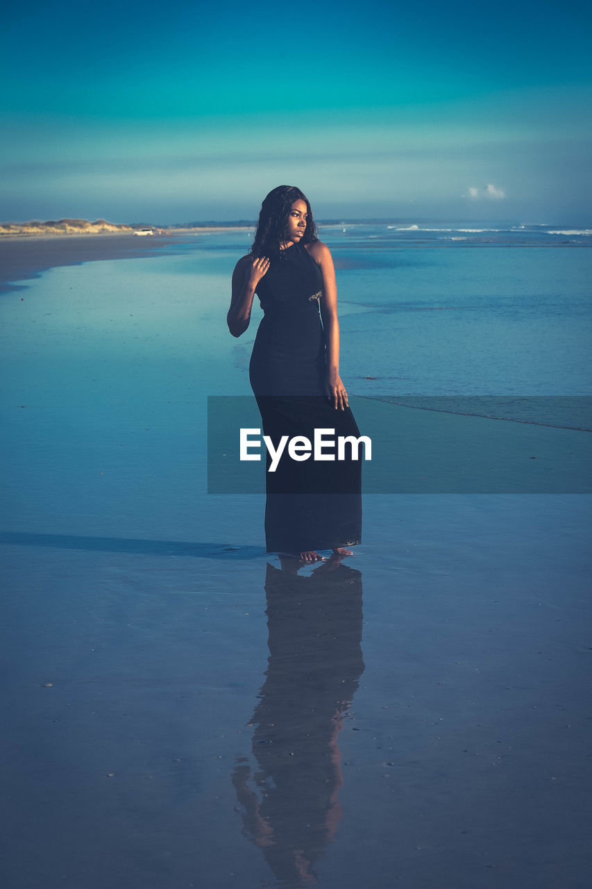 Full length of young woman standing on shore at beach