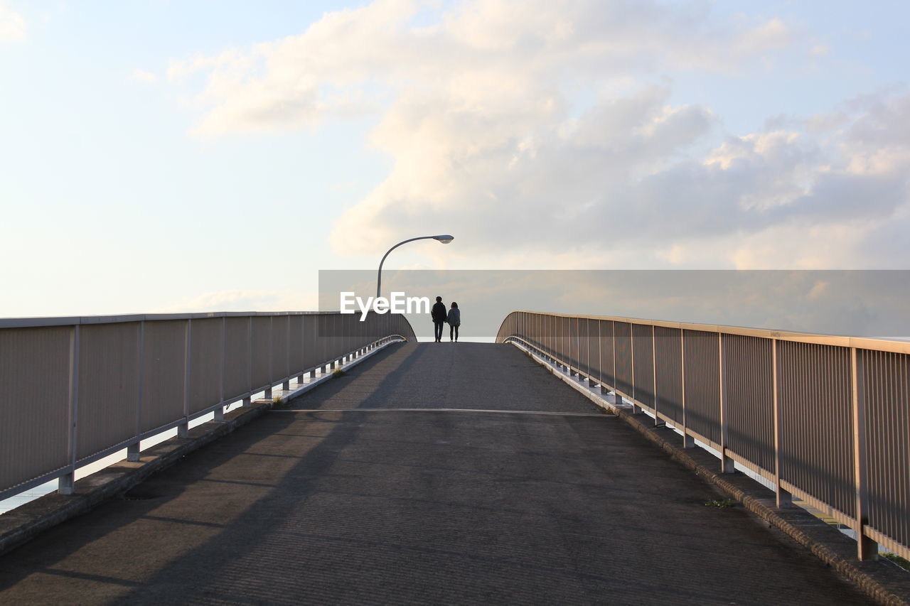 Rear view of friends walking on footbridge against sky