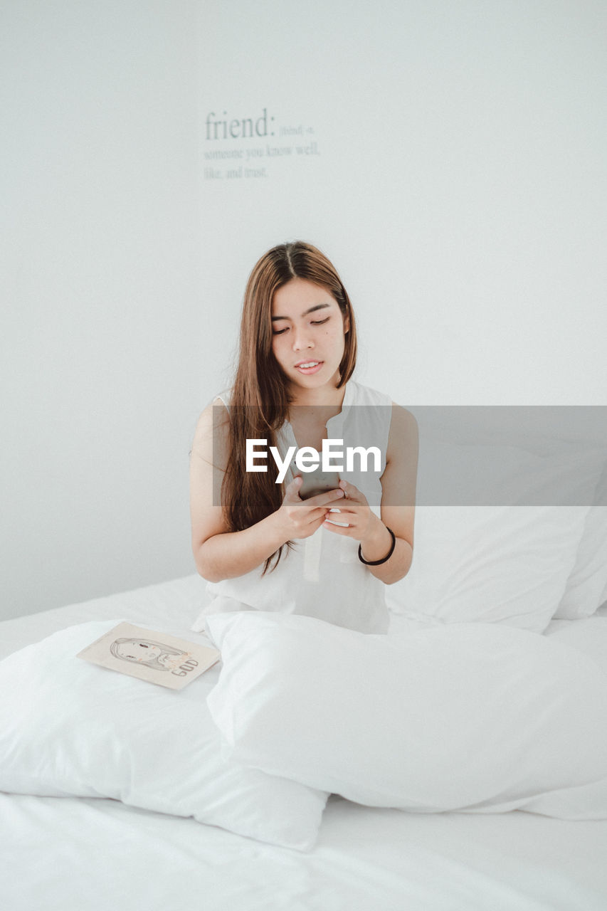 YOUNG WOMAN USING MOBILE PHONE IN BED