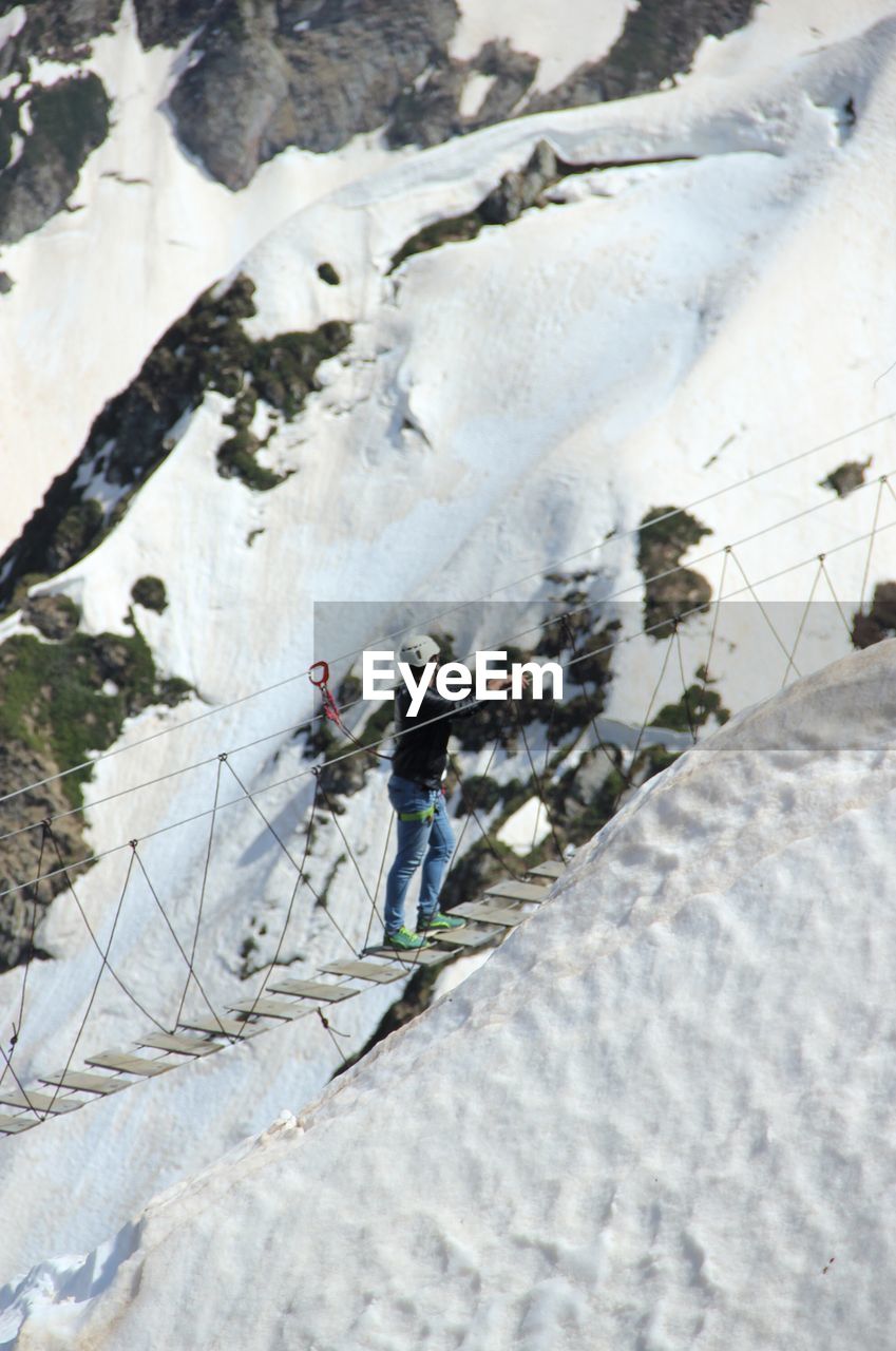 High angle view of man walking on footbridge by snow covered mountains