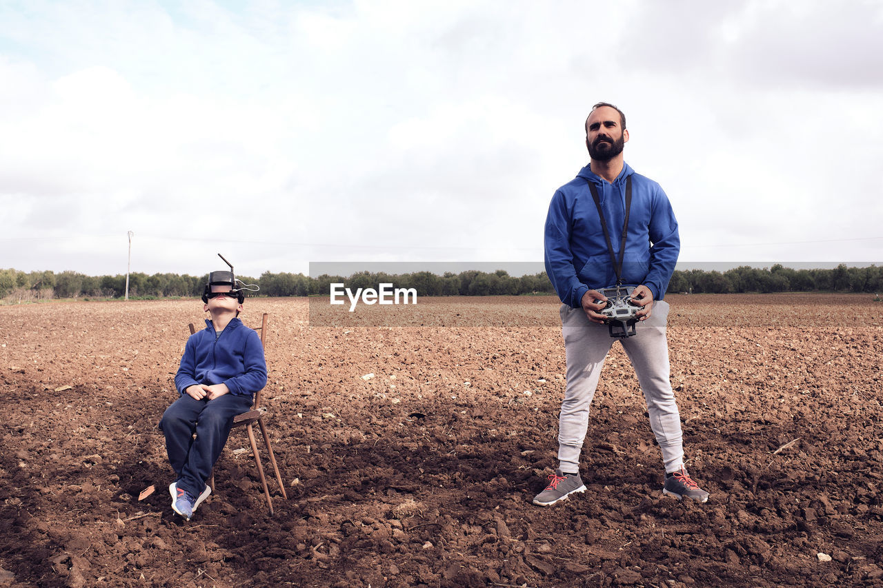 Young man in the field teaches his son how to fly a drone