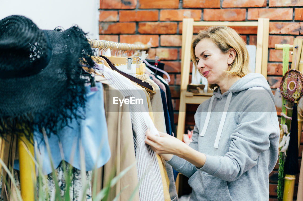 Woman shopper with a smile chooses fashionable clothes on hangers in a boutique.