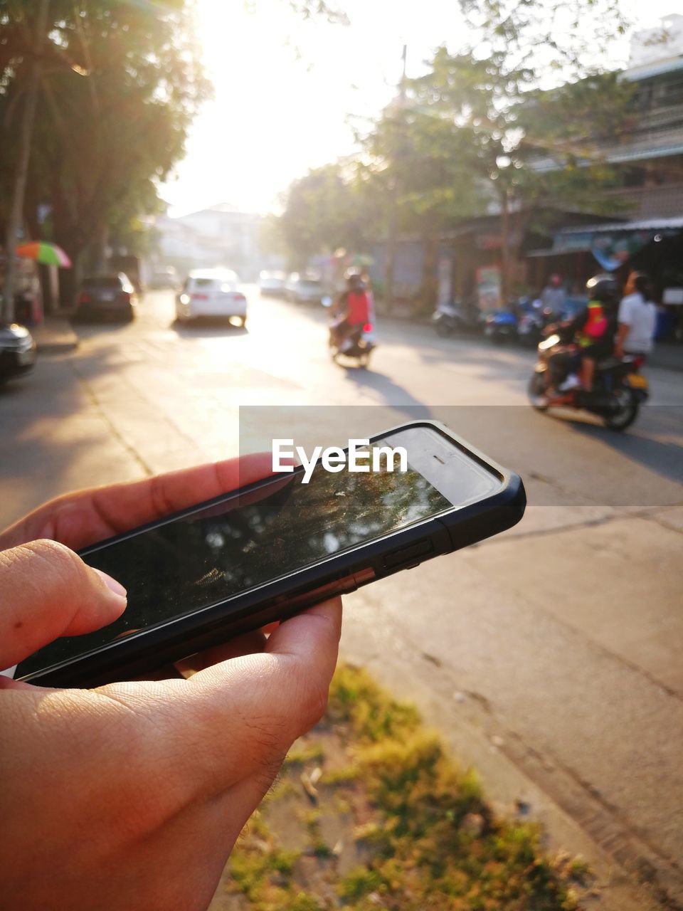 CLOSE-UP OF MAN HOLDING MOBILE PHONE ON ROAD