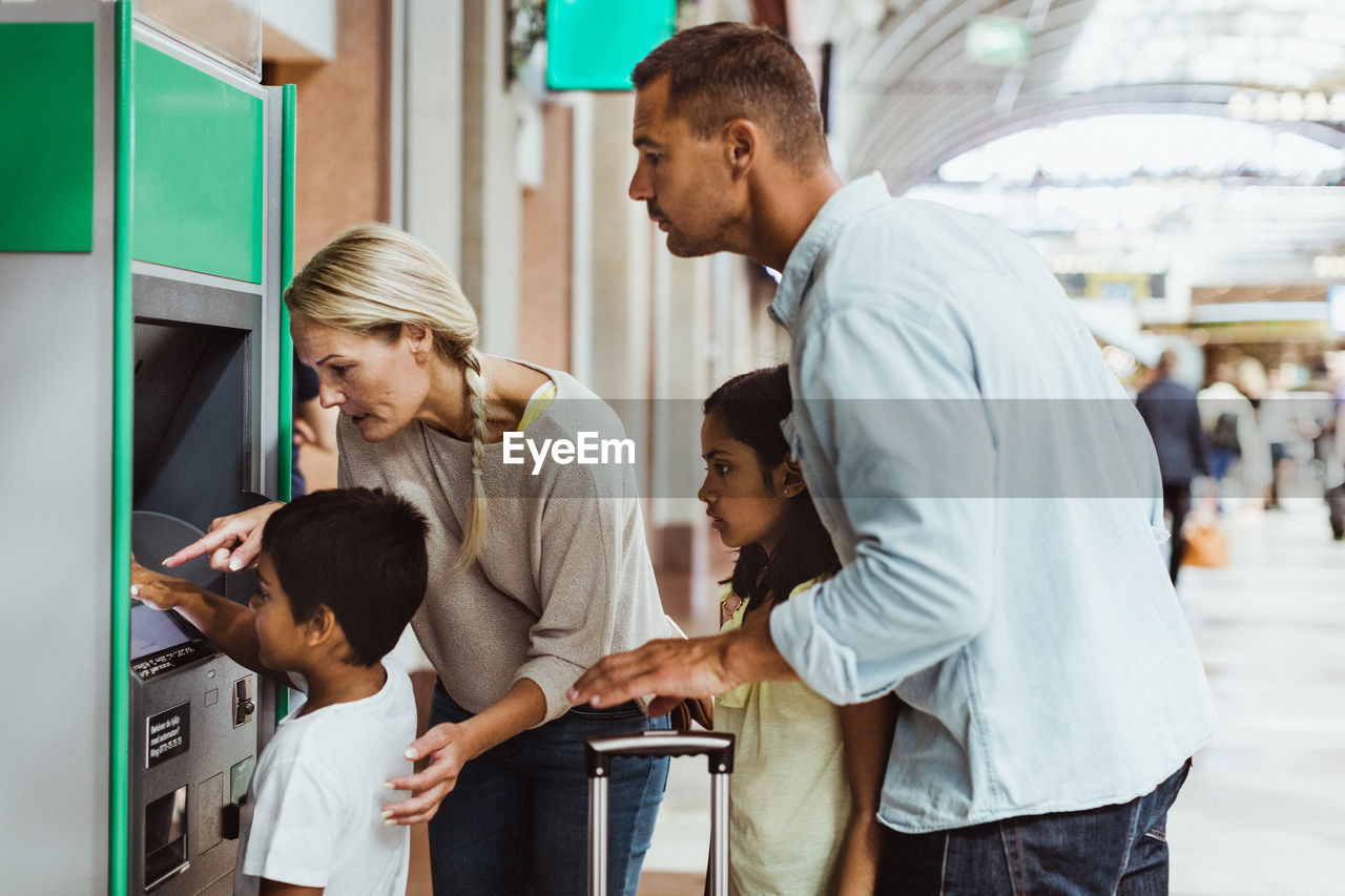 Family looking at boy buying ticket on railroad station platform