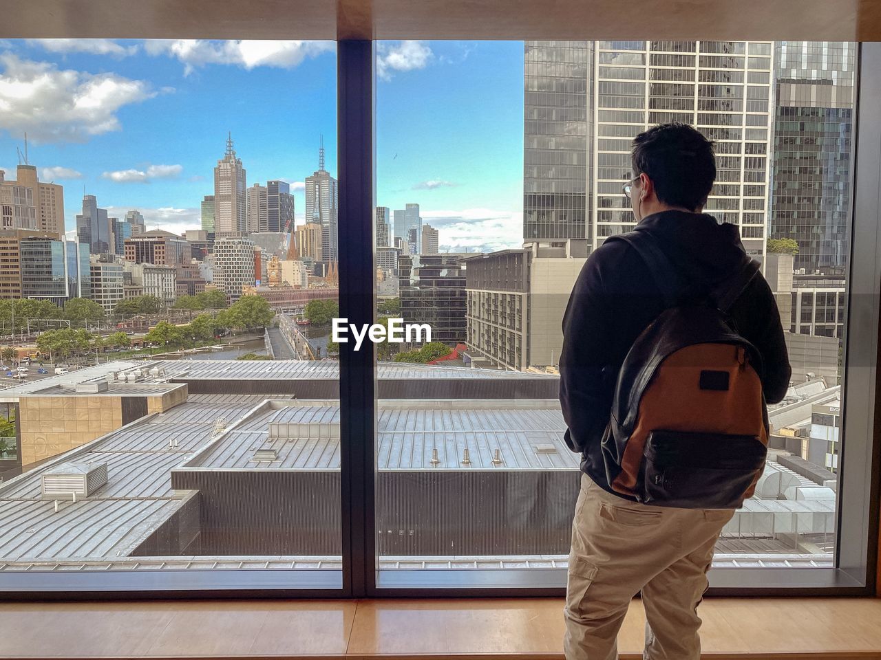 Rear view of man looking at window view of buildings and urban skyline.