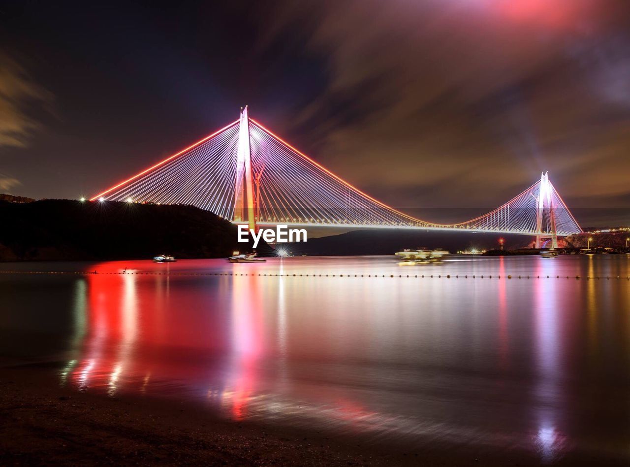 Illuminated cable-stayed bridge over river against sky at night