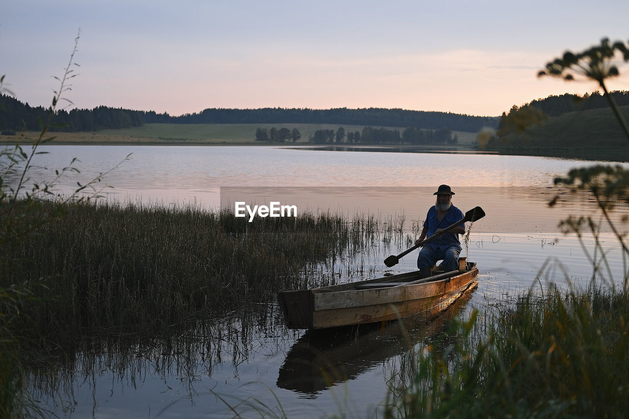 MAN IN LAKE AGAINST SKY AT SUNSET