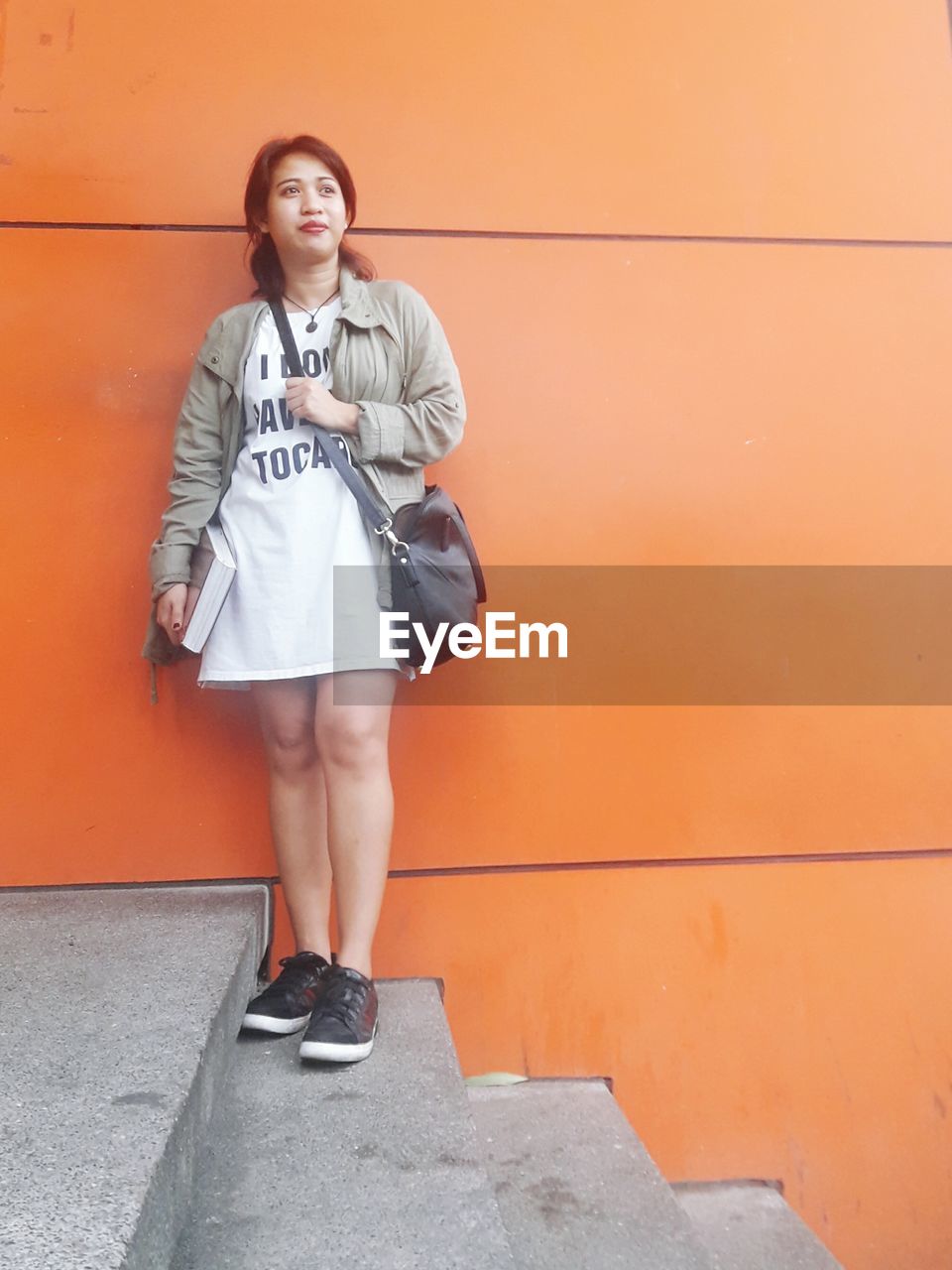 Young woman standing on steps against orange wall