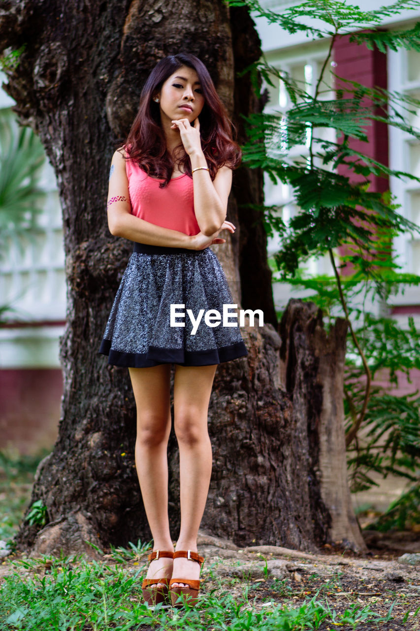 Portrait of young woman standing against tree trunk