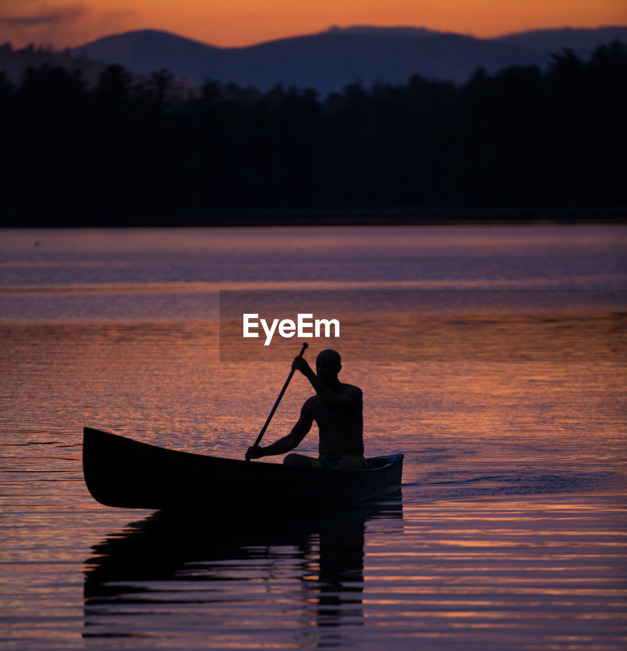 Silhouette man on boat in lake against sky during sunset