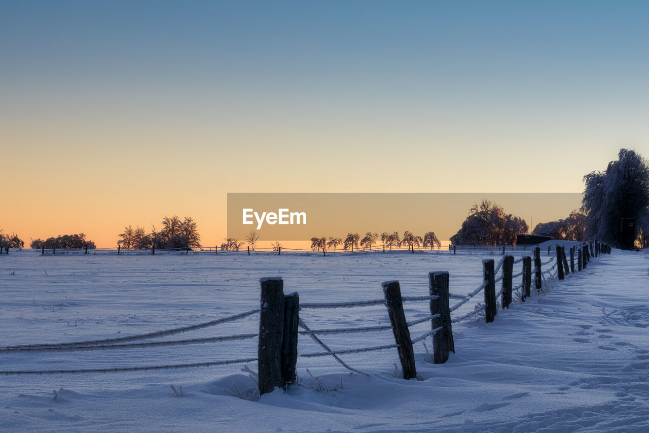 WOODEN FENCE ON SNOW COVERED FIELD AGAINST CLEAR SKY