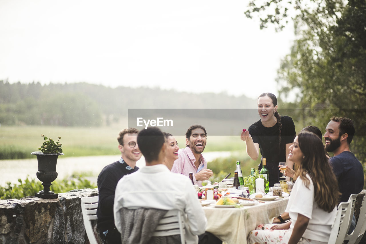 Cheerful male and female friends enjoying dinner party in backyard during weekend