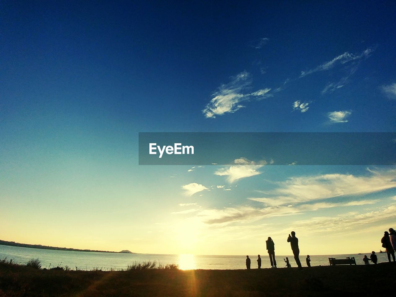 SILHOUETTE PEOPLE STANDING ON BEACH AGAINST BLUE SKY