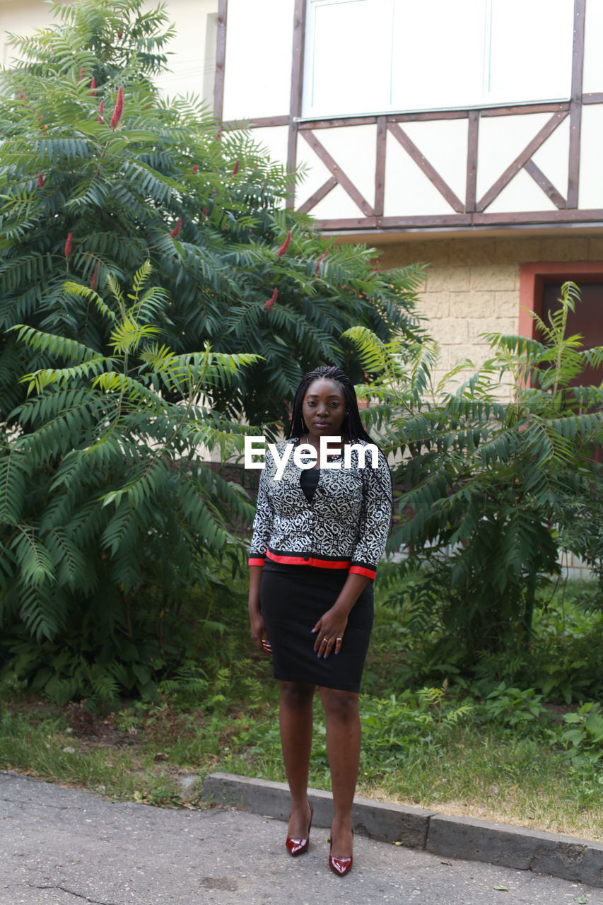 PORTRAIT OF WOMAN STANDING AGAINST PLANTS