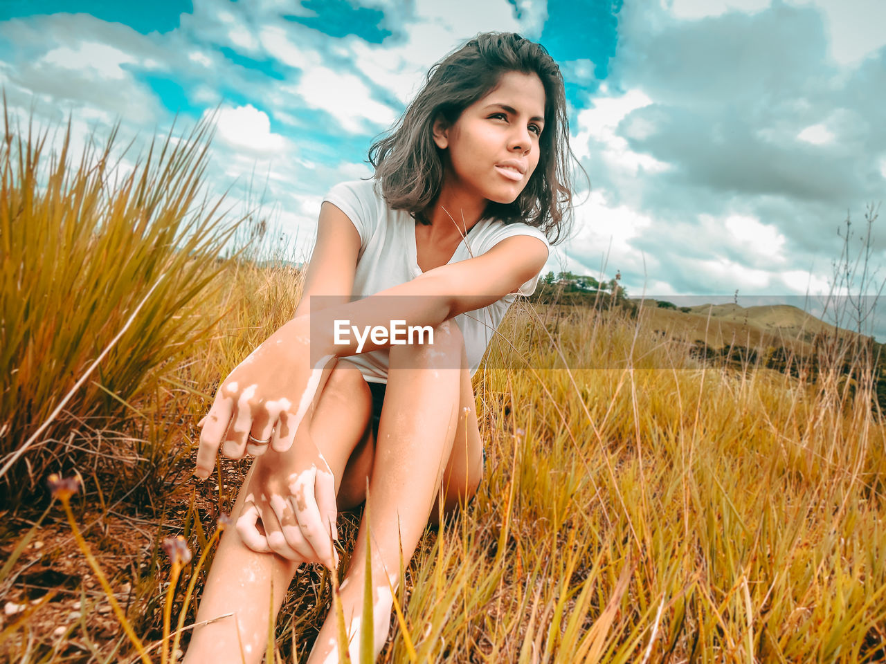 Young woman sitting on field against sky