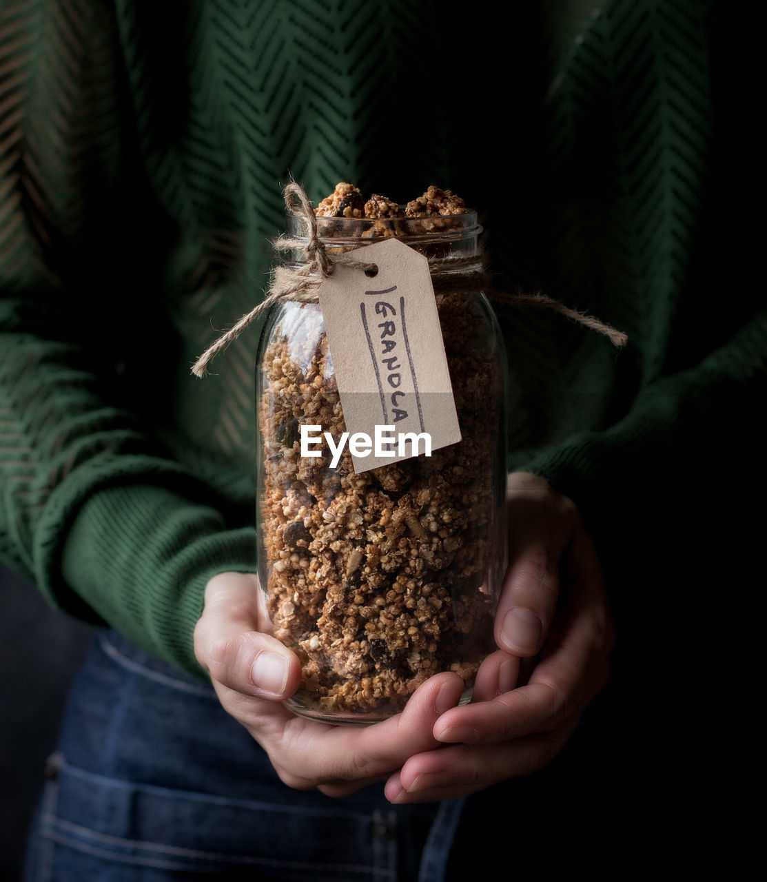 Unrecognizable female carrying glass jar of fresh millet and quinoa granola with label