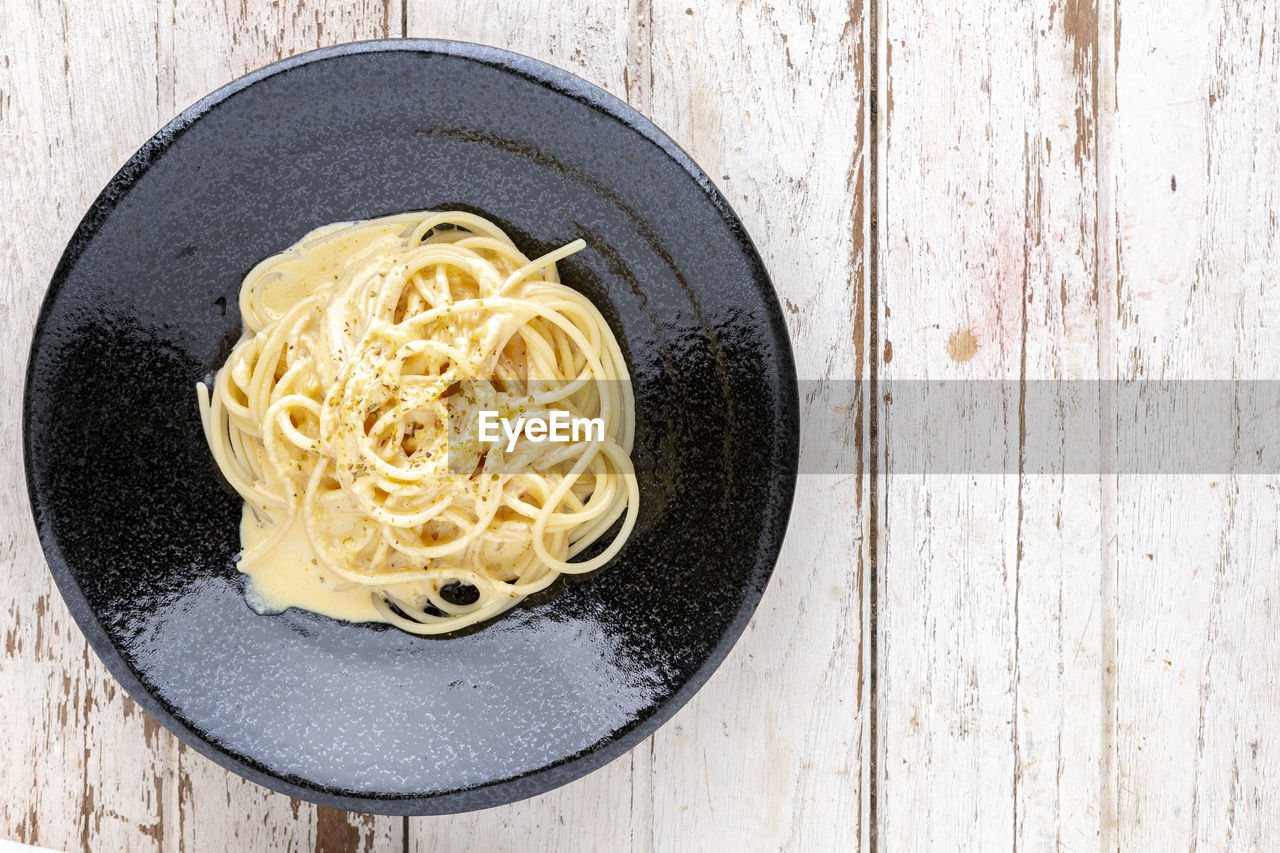 Spaghetti carbonara with cream sauce and oregano on top in black ceramic plate, top view