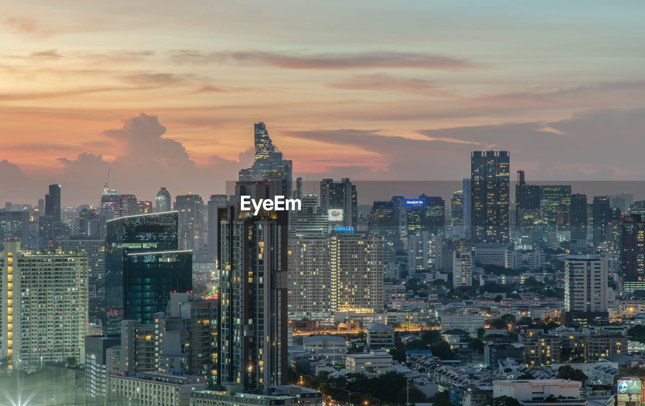 AERIAL VIEW OF ILLUMINATED BUILDINGS AGAINST SKY DURING SUNSET