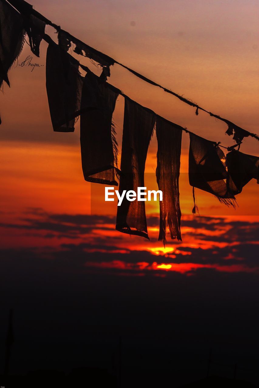 Prayer flag hanging on clothesline against an orange sky