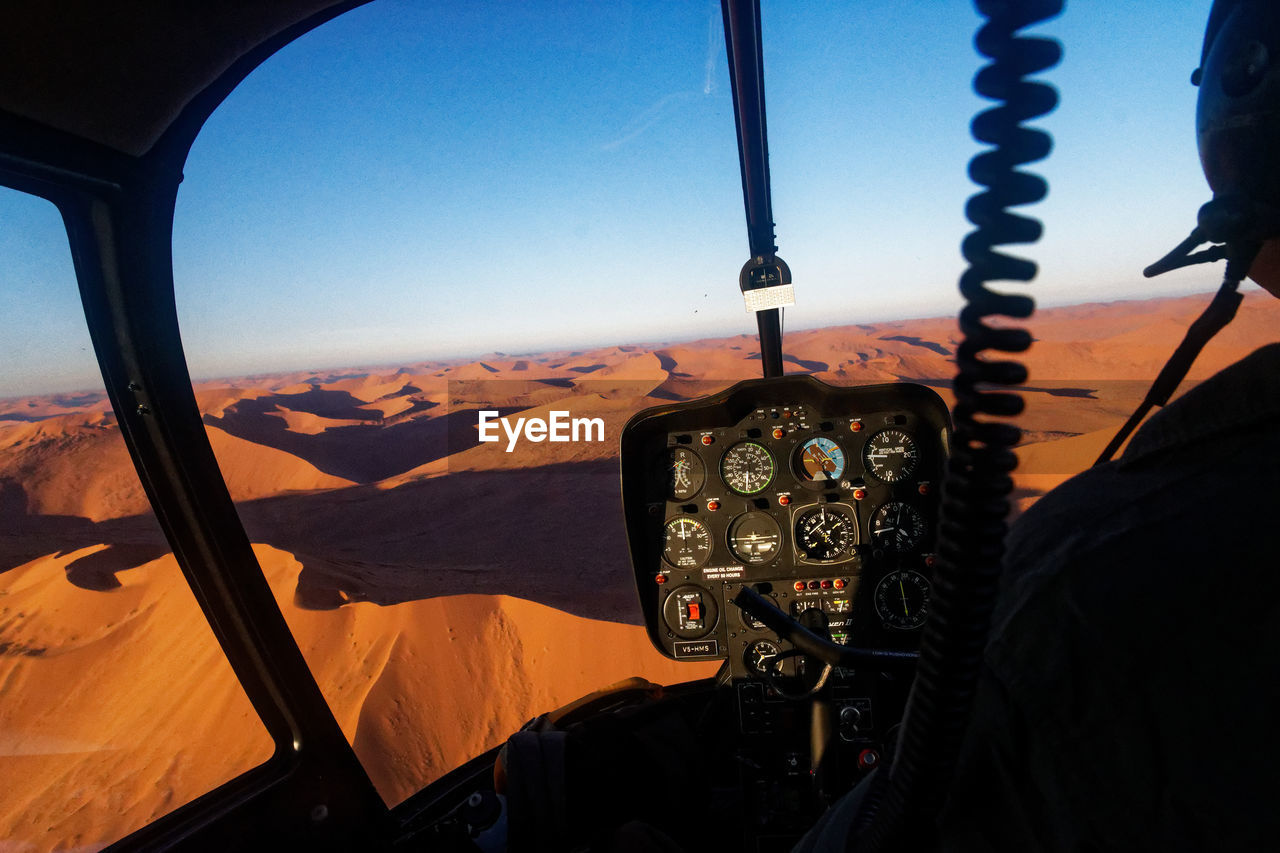 Cropped image of pilot flying airplane at desert against clear blue sky