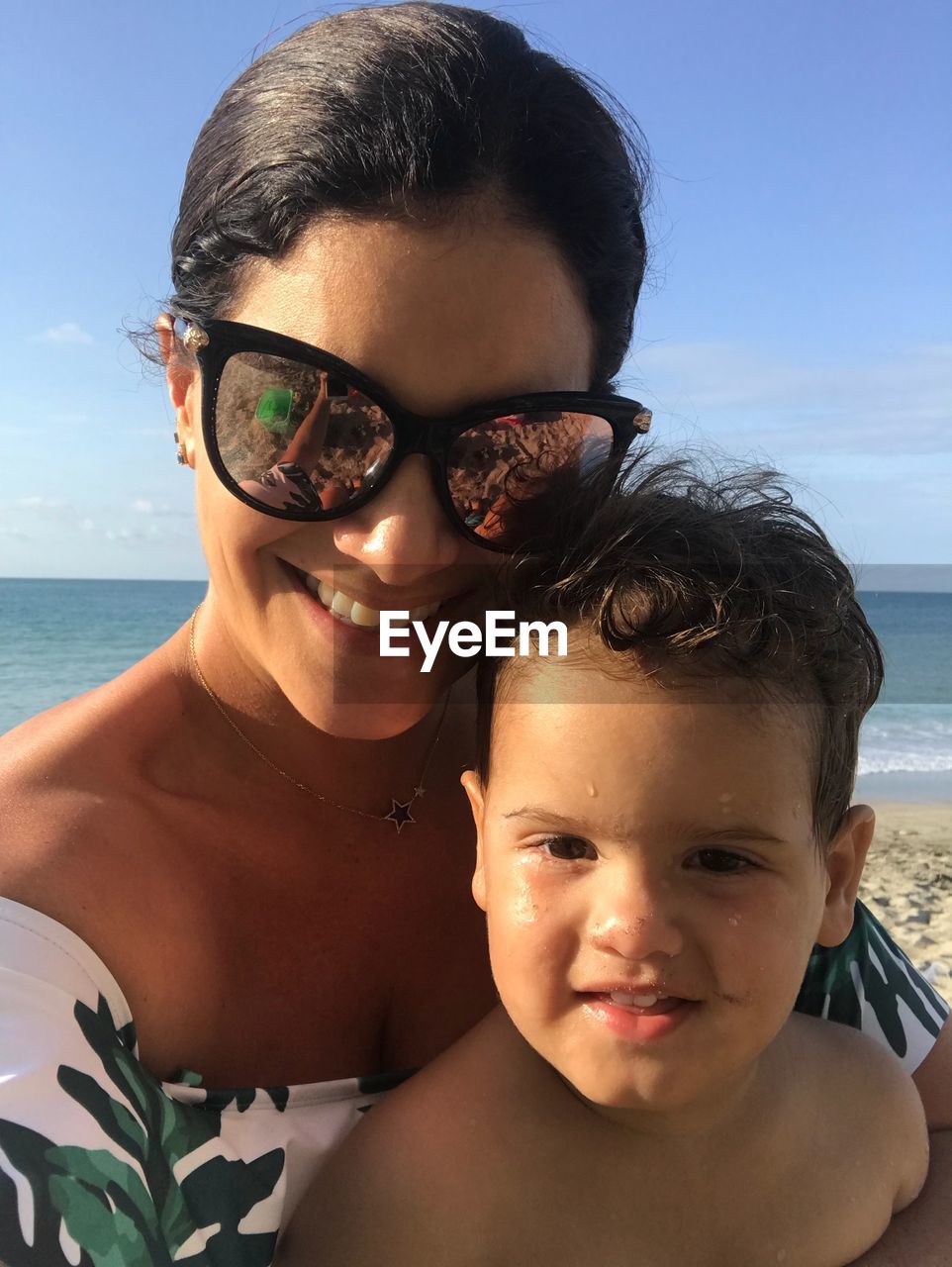 Portrait of smiling mother and son at beach against sky