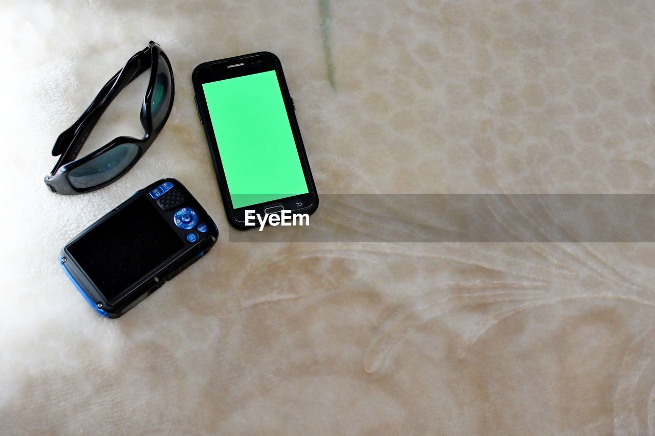 High angle view of smart phone with digital camera and sunglasses on table