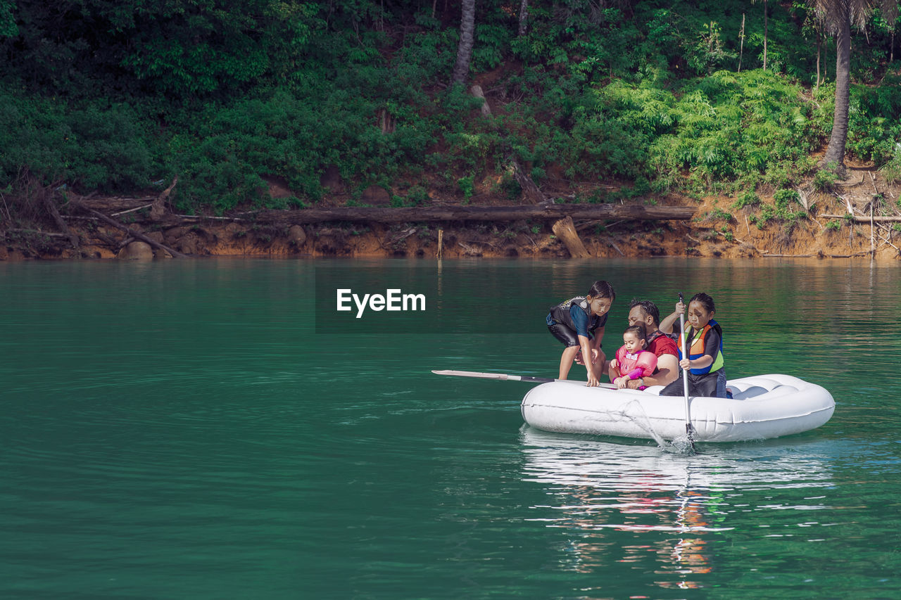 Family wearing life jackets paddling on an inflatable boat in kenyir lake, malaysia.