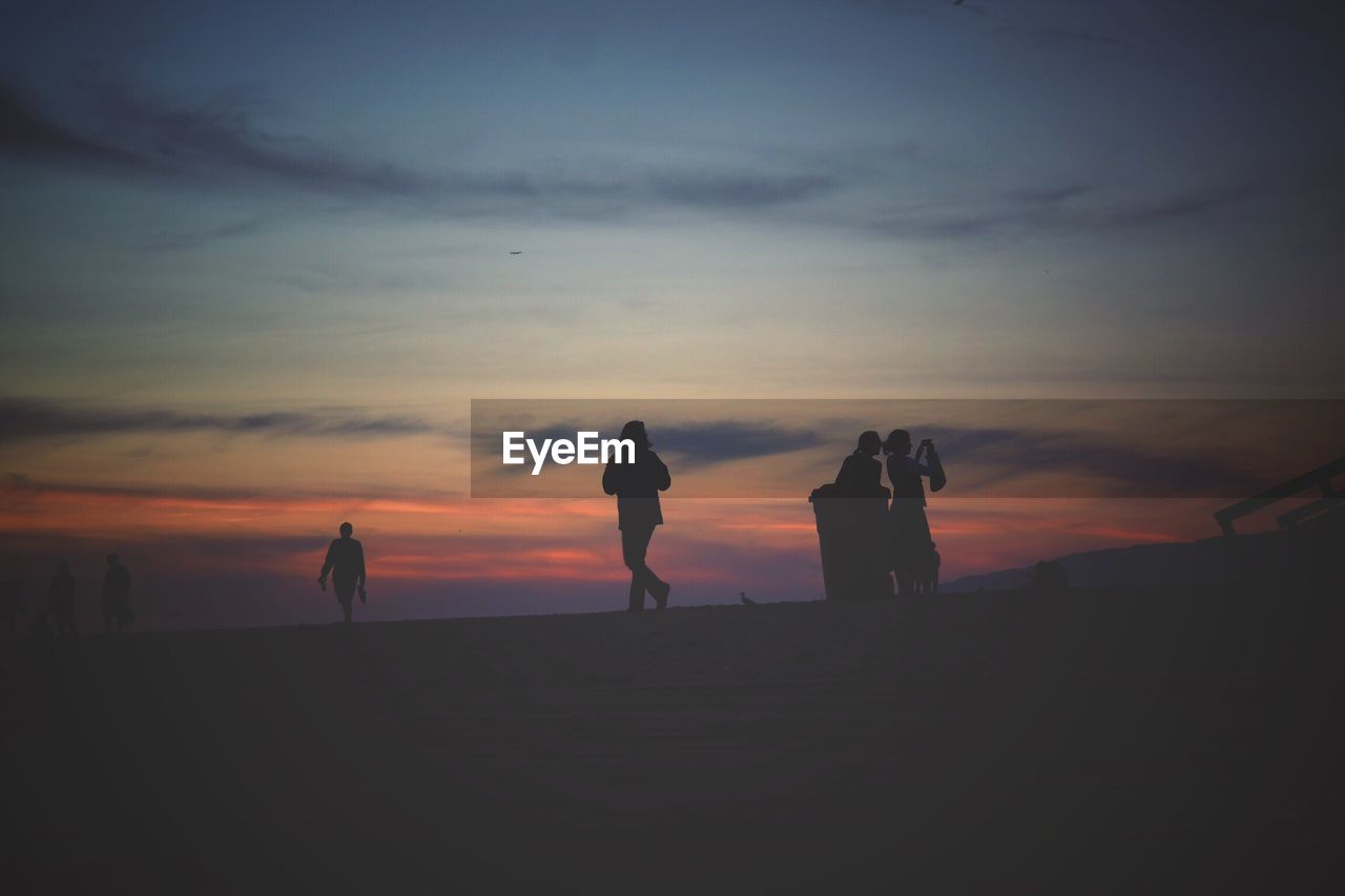 SILHOUETTE PEOPLE STANDING AT BEACH AGAINST SKY DURING SUNSET