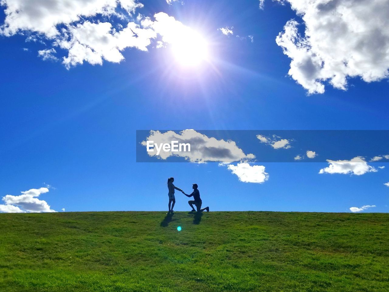 Man proposing woman on field against sky