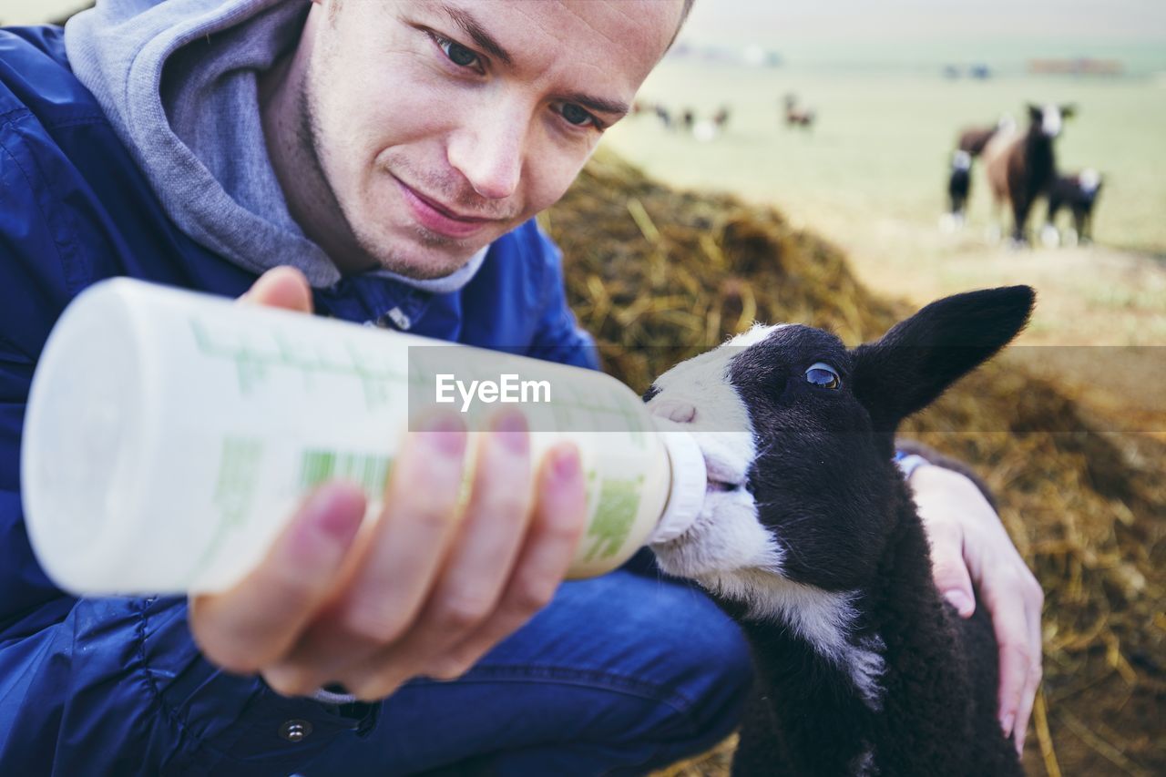 Smiling mid adult man feeding milk to lamb