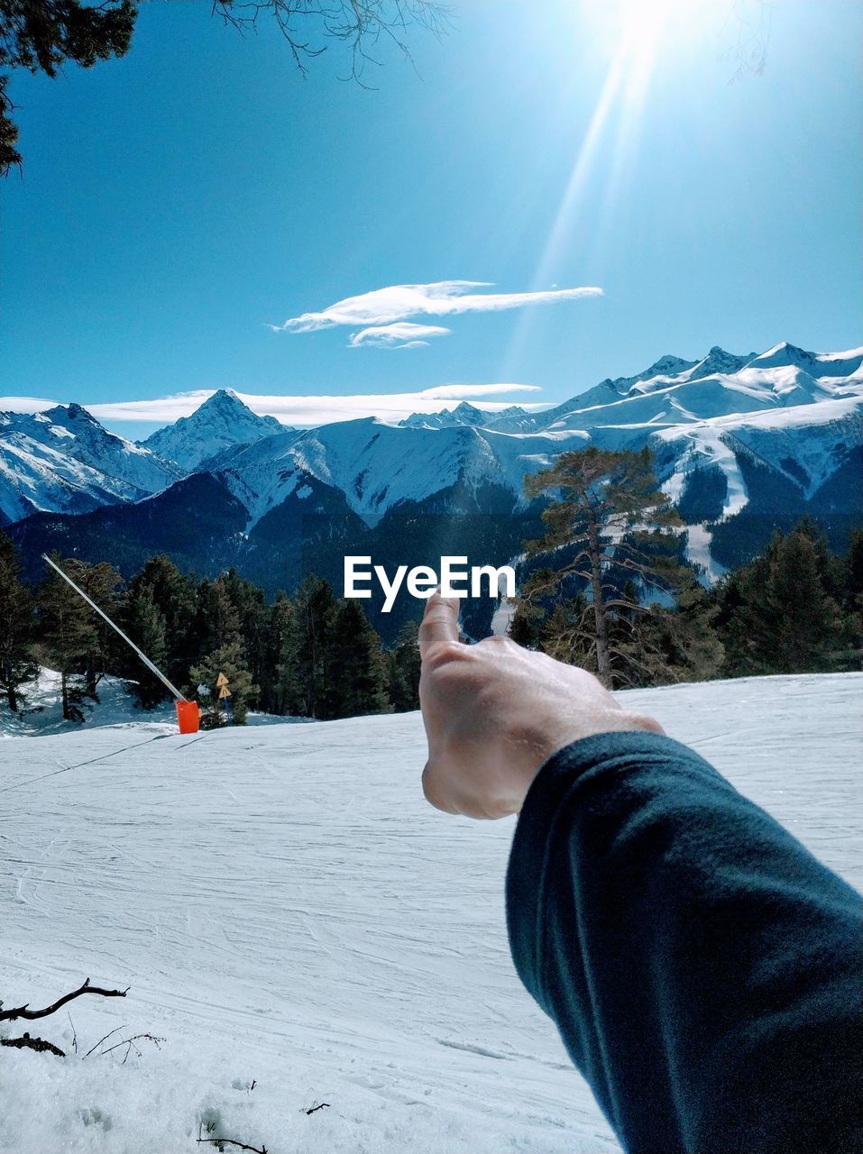 Cropped hand of person pointing towards snowcapped mountain against sky