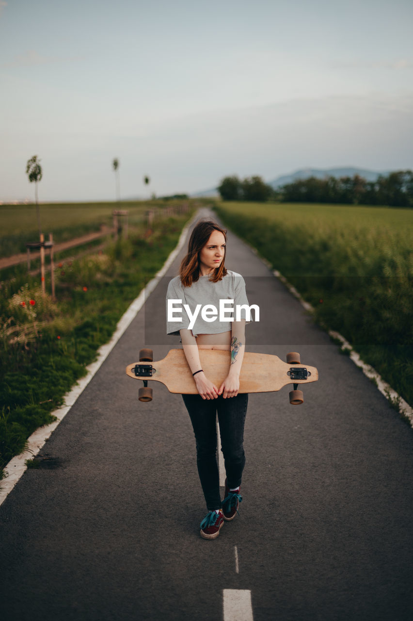 Young woman holding skateboard standing on road