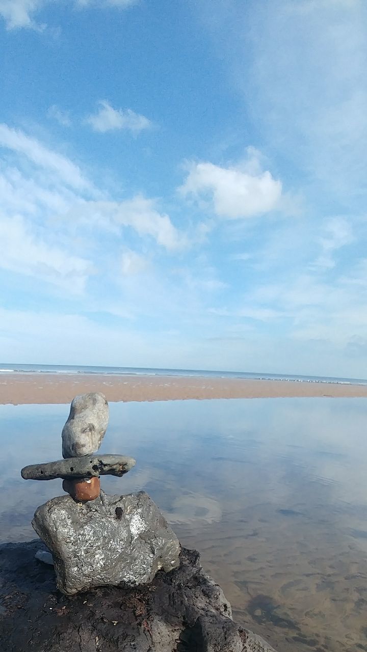 Stack of stones by sea against sky