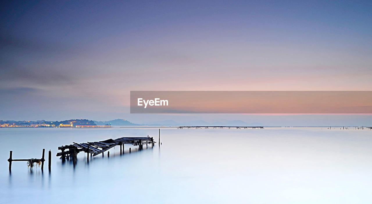 Old pier on sea against sky at sunset