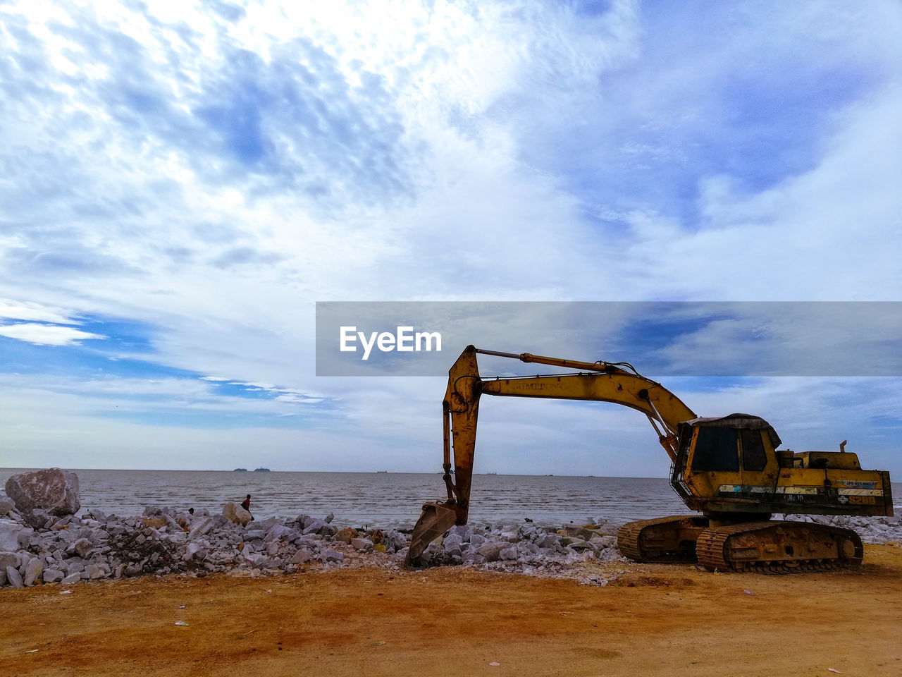 Bulldozer at beach against cloudy sky