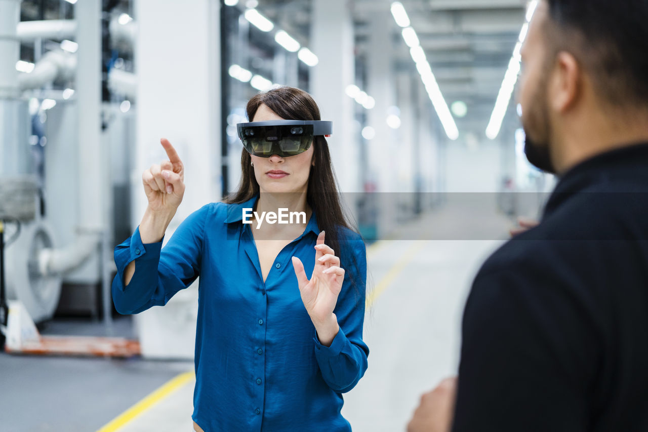 Businesswoman with augmented reality glasses explaining to engineer in industry