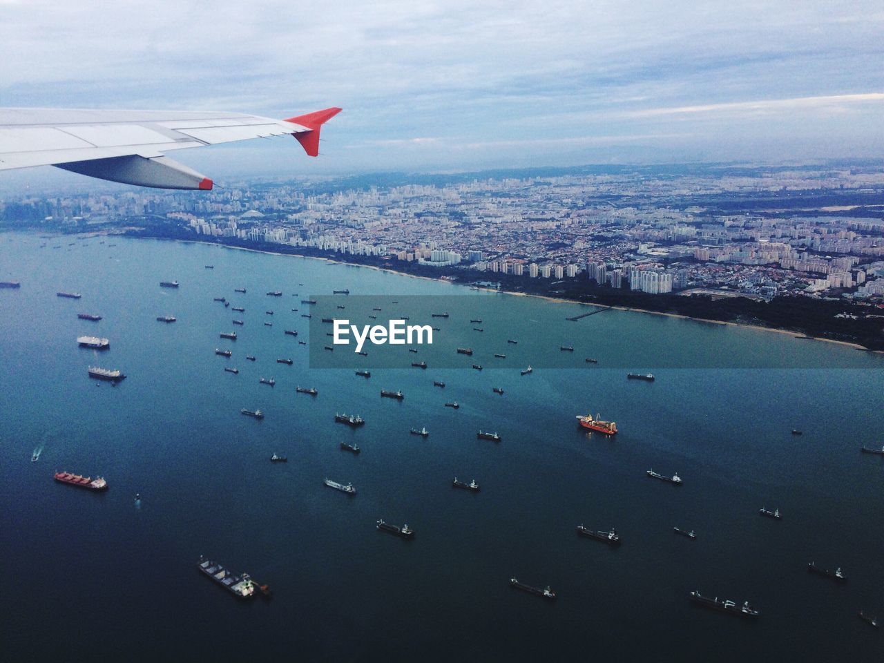 AERIAL VIEW OF AIRPLANE FLYING OVER SEA AGAINST CITYSCAPE